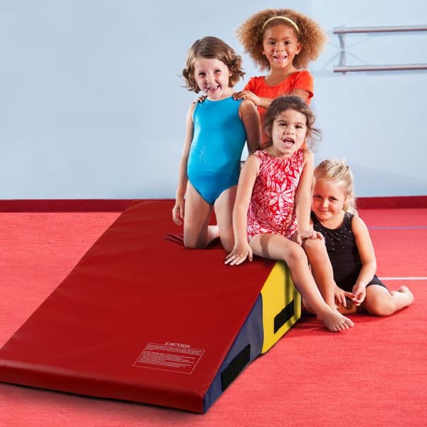 Red incline mat with yellow and blue sides, four children sitting on it in a gym