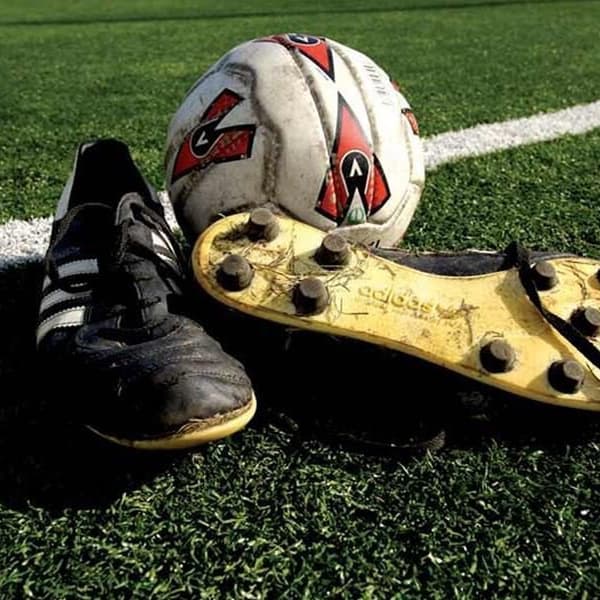 Artificial turf rolls on an outdoor field with soccer shoes and a soccer ball.