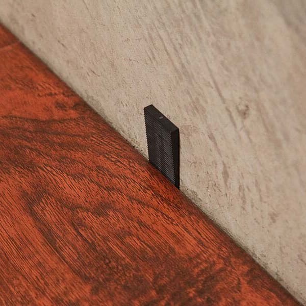 Black hard plastic flooring spacer between red wood-look flooring and beige wall