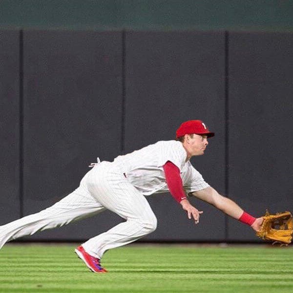 Baseball field with player diving for ball, dark gray wall pads on back wall