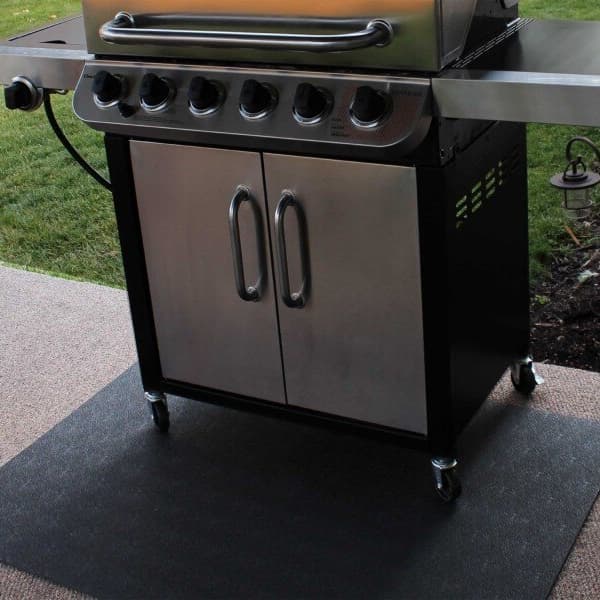 Black utility mat under a stainless steel grill on a textured patio surface