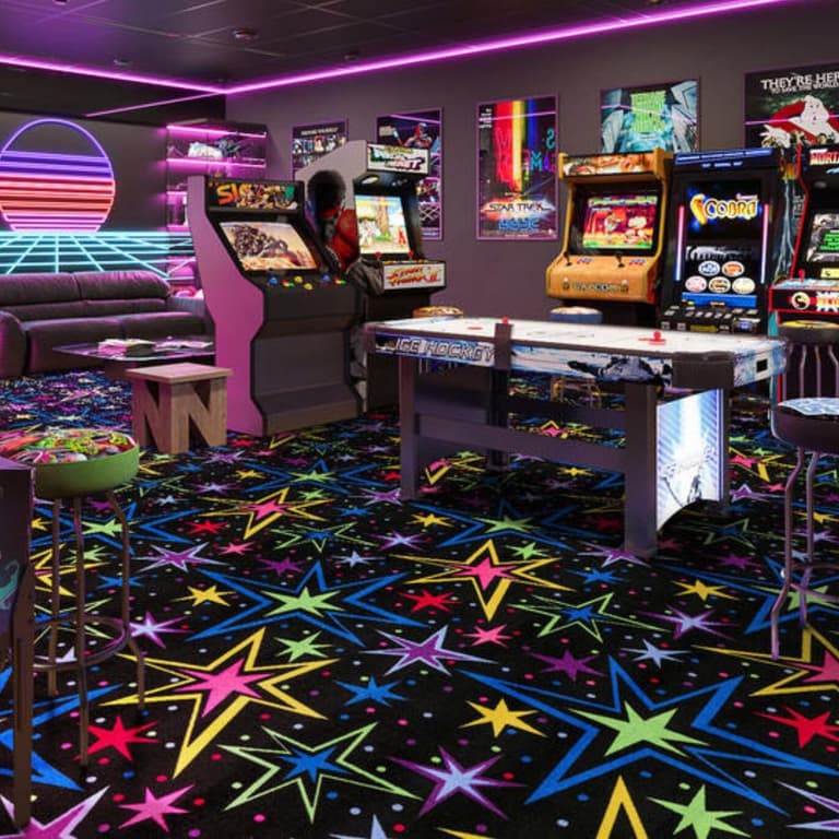 Joy Carpets Neon Lights Carpet — Kapow, vibrant multicolor starburst pattern on black background, in a retro arcade room