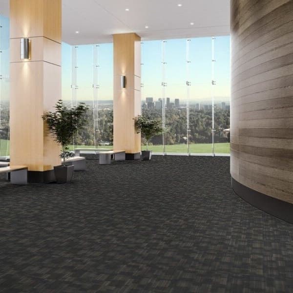 J&J Flooring Evolve Carpet Tile, Amalgam — modern office lobby with dark gray textured carpet tiles under large windows and