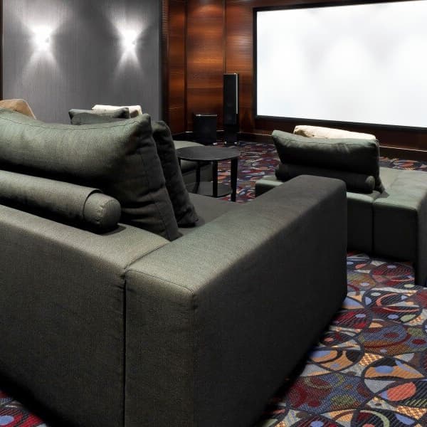 Joy Carpets Futura Carpet, Salsa — home theater room with patterned nylon carpet under dark gray sectional sofa and media