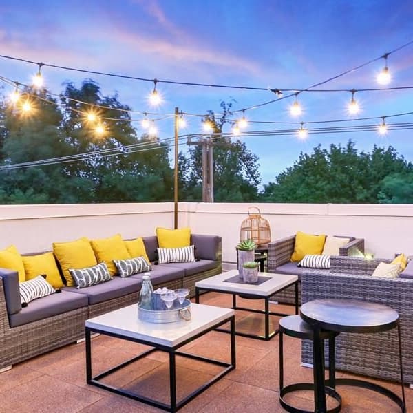 Rooftop deck with interlocking rubber tiles in brown, furnished with wicker seating and string lights at dusk