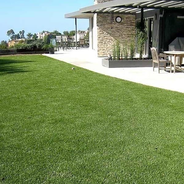 Artificial turf rolls in a landscaped backyard with outdoor seating.