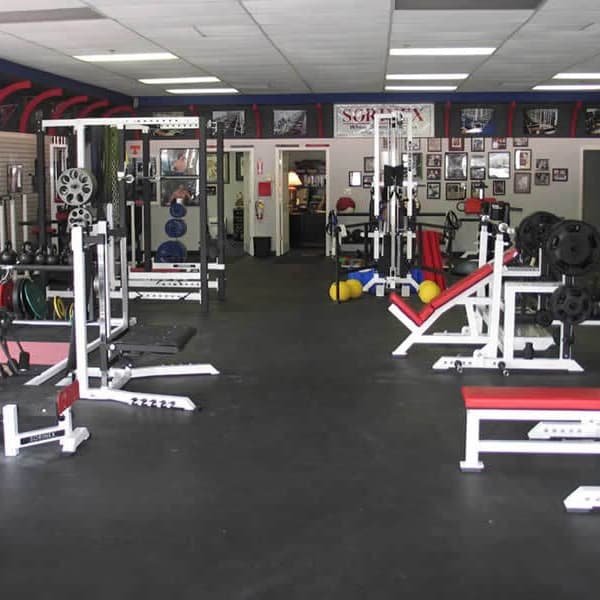 Rubber floor tiles in commercial gym with squat racks, benches, and colorful weight plates.