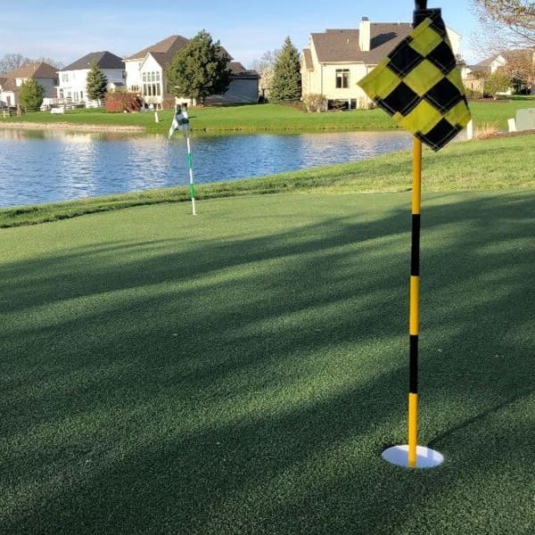 Putting green turf rolls on a golf course with cup flags and overlooking a lake and houses.