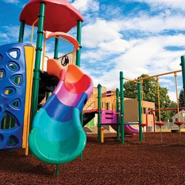 Playground with colorful equipment and brown shredded rubber mulch flooring under a blue sky