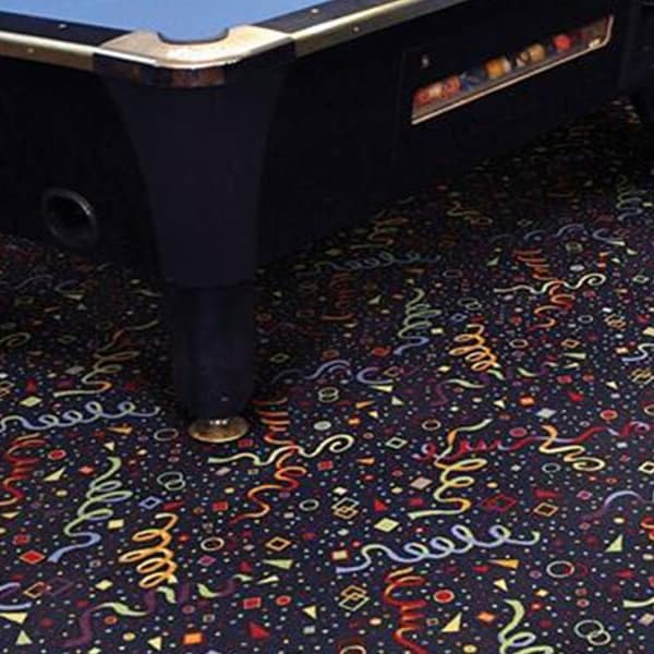 Shaw Ticker Tape II Carpet, Confetti Toss — dark carpet with colorful streamer and confetti pattern under a pool table