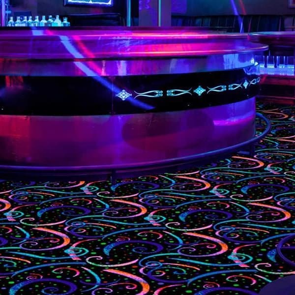 Joy Carpets Neon Lights Carpet Dynamo — vibrant multicolor swirl pattern on black background in a bar with purple lighting