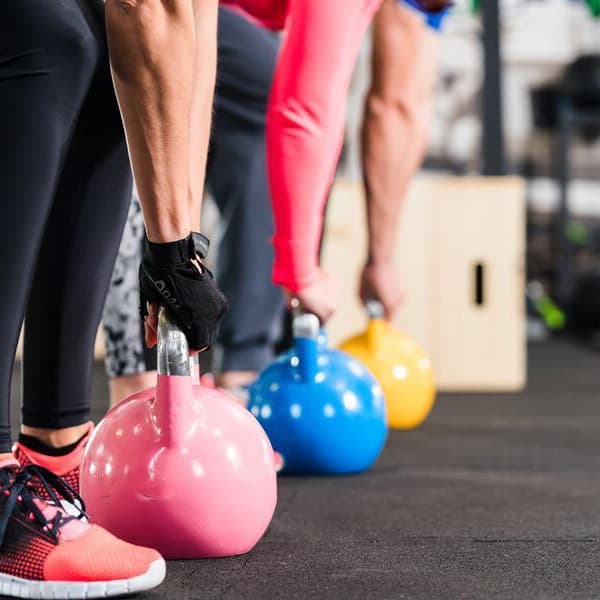 Three people lifting kettlebells in gym with black interlocking rubber tiles.