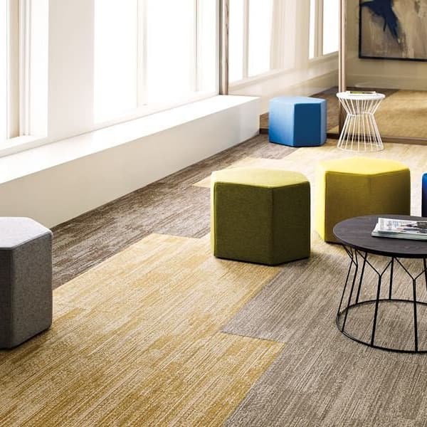 Shaw Rhythm carpet tiles in a modern lounge with hexagonal ottomans and wireframe tables
