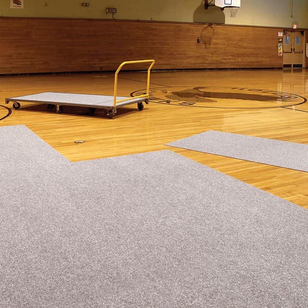 Gray gym floor cover tiles partially laid on a wooden basketball court