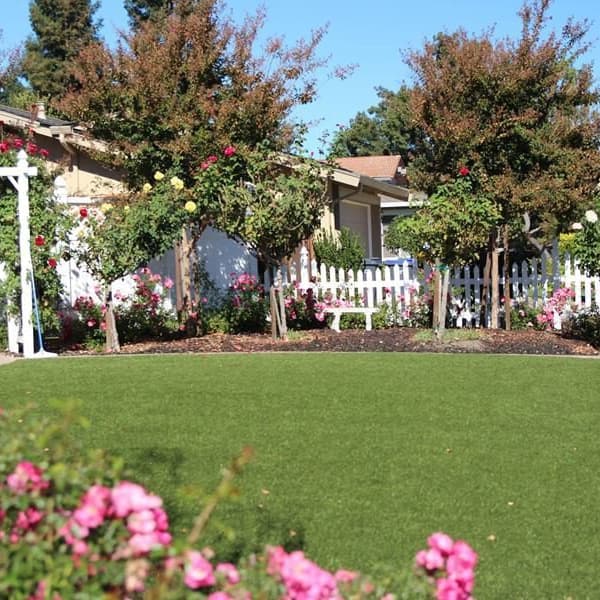 Monterey Turf Rolls — Emerald/Olive Green artificial grass in landscaped backyard with flowers and white picket fence