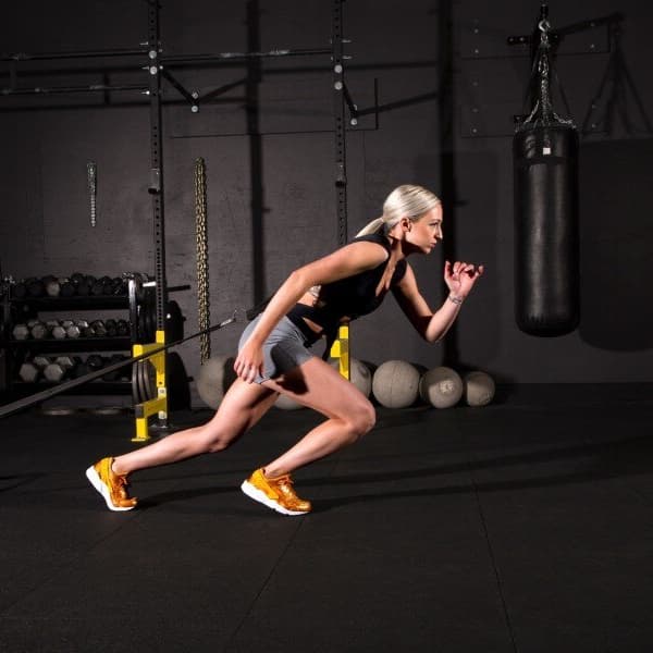 Home gym with black Rebound Rubber Tiles, woman performing sled push exercise