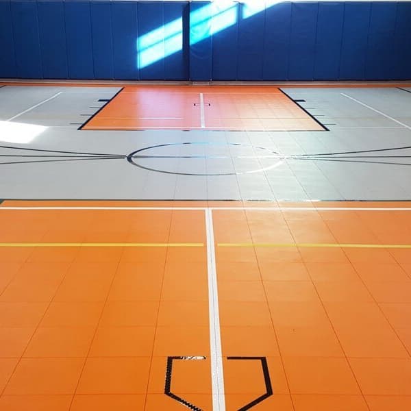 Indoor gymnasium with orange and gray premium sports tiles, court lines, blue padded walls