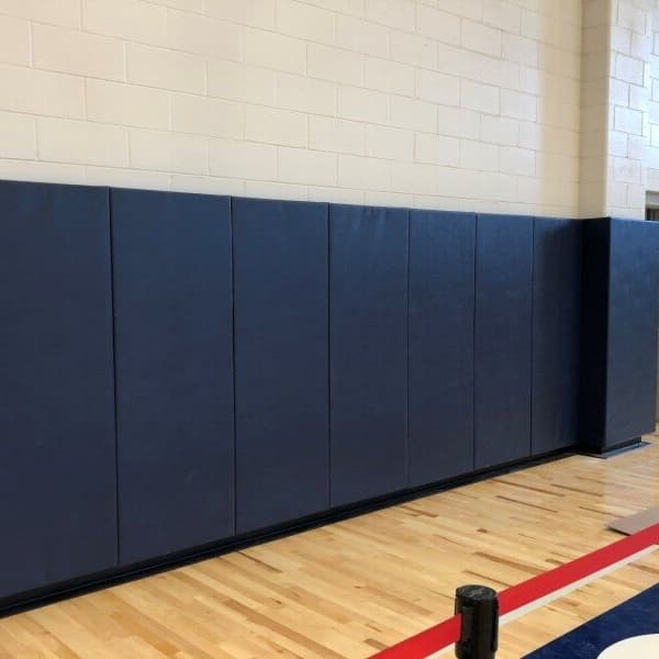 Navy blue 2' x 4' safety wall pads installed along a gymnasium wall, covering a cream-colored brick surface