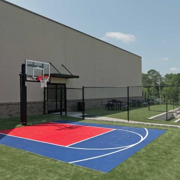 Outdoor basketball court with red and blue VersaCourt Boost Tiles installed on grass