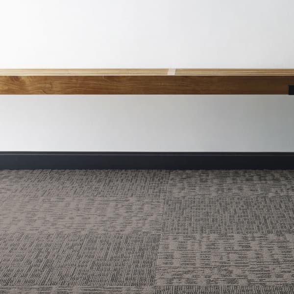 Shaw Genius Carpet Tile, Scholarly — low-angle view of gray textured carpet tiles under a wooden bench in an office setting