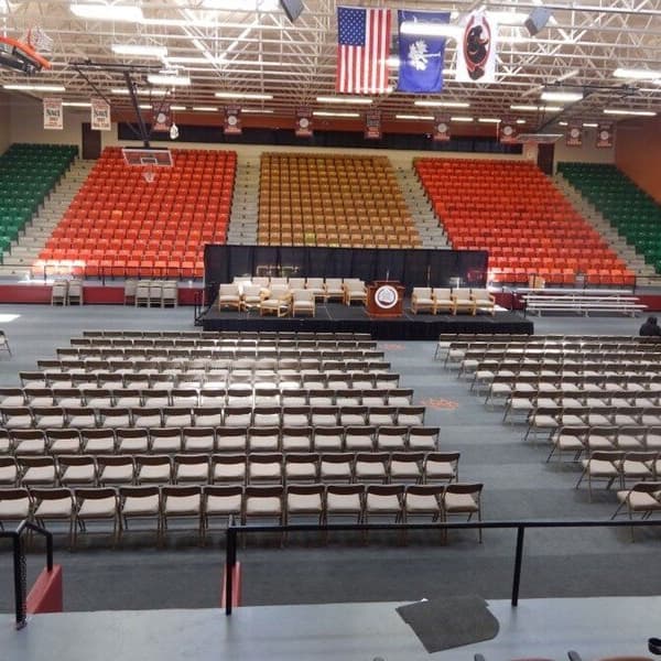 Rubber tiles in an indoor arena set up for a graduation or assembly event, with folding chairs and colorful stadium seating.