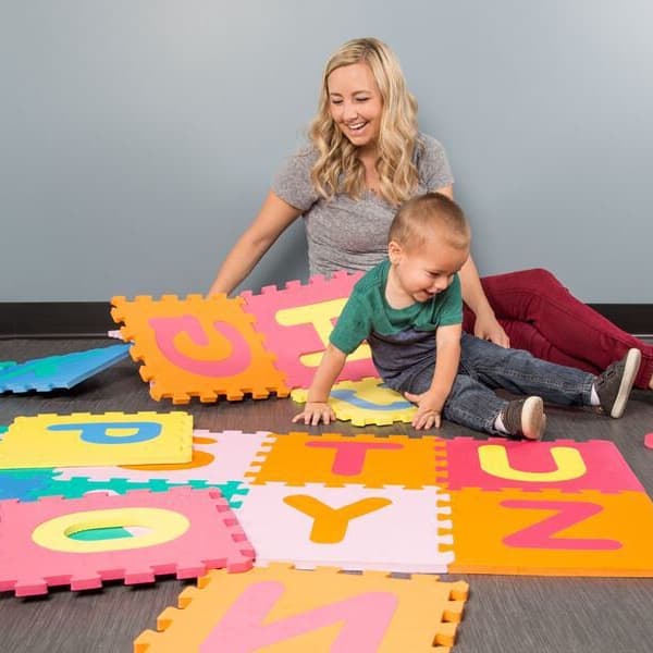 Colorful foam alphabet tiles scattered on a dark floor with a woman and child playing