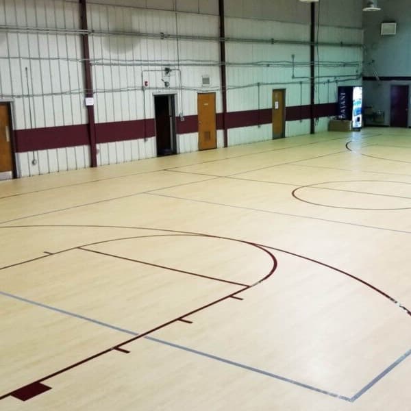 Indoor basketball court with maple luxury vinyl tile flooring and maroon court lines in a gymnasium