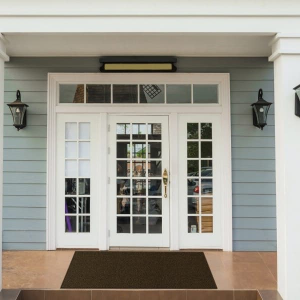 Front porch with white double doors and light blue siding, featuring a dark brown walk off carpet tile at the entrance