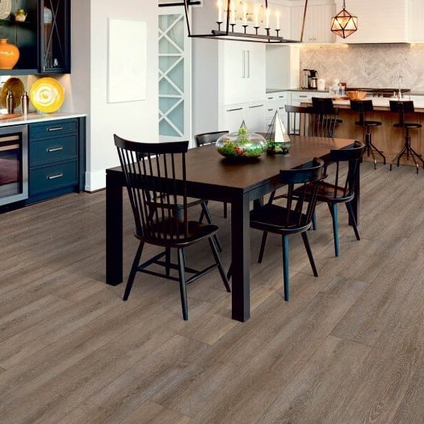 Waterproof vinyl planks in an open layout kitchen and dining room with wood furniture and white cabinetry.