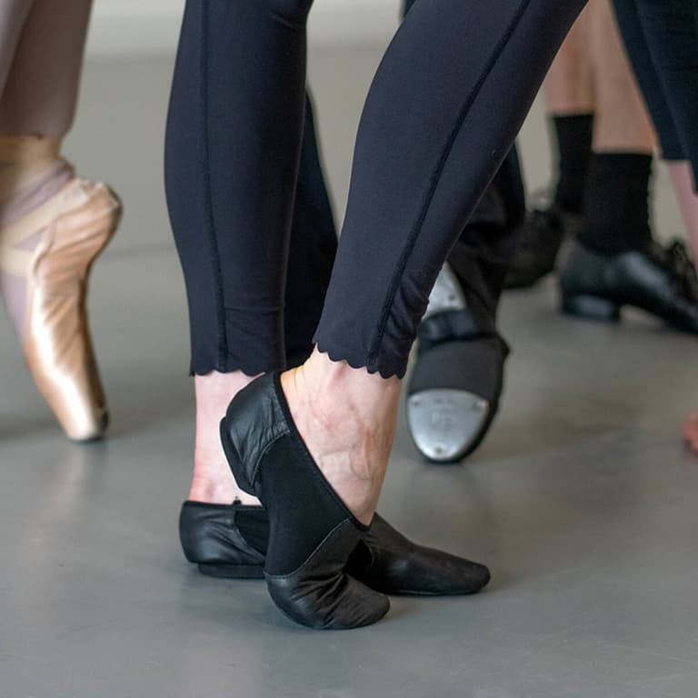 Close-up of dancers' feet in ballet, jazz, and tap shoes on gray flooring
