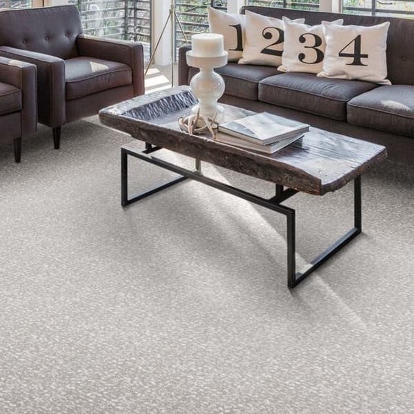 Living room with Joy Carpets Lazy Day Carpet in Mist, under a dark sofa, two armchairs, and a rustic coffee table