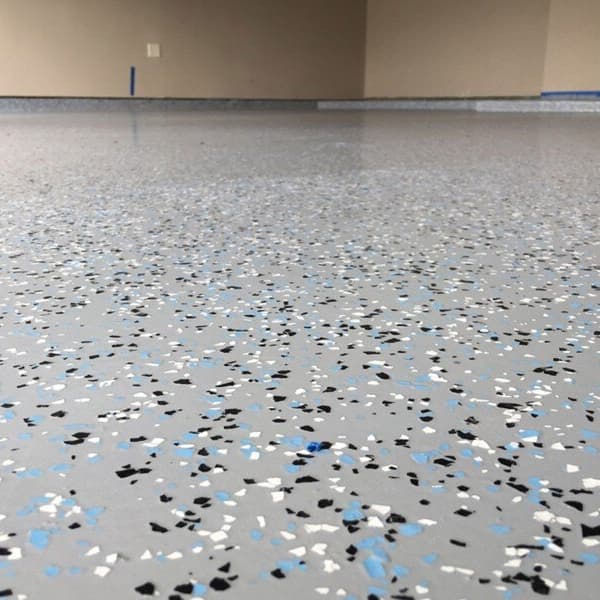 Close-up of light gray epoxy garage floor coating with decorative black, white, and blue color flakes.