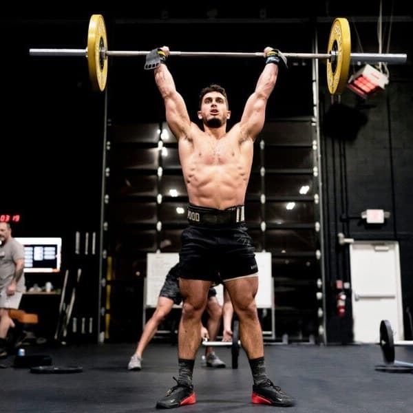Athlete lifting a barbell overhead in a gym with black rubber flooring.