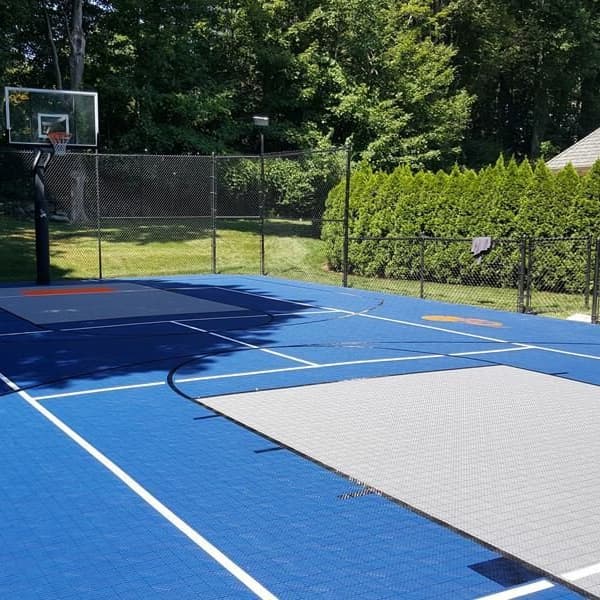 Outdoor basketball court with Mateflex III Court Tiles in Performance Blue and Stone Gray, featuring white lines and a hoop