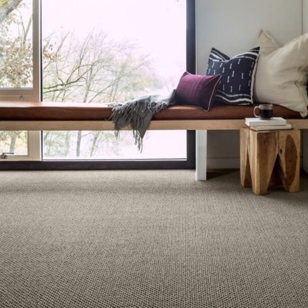 Dark textured carpet flooring in modern living space with wooden bench seating and decorative pillows in front of window.