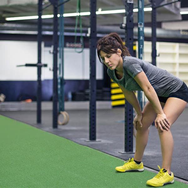 Turf in a functional fitness gym with woman resting after workout with squat racks and equipment in the backyard.