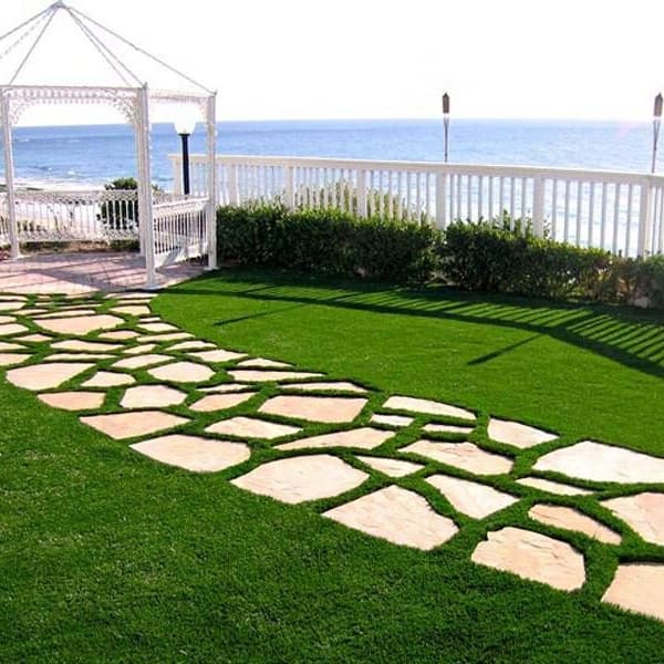 Artificial turf rolls with stone walkway and white gazebo by the ocean.