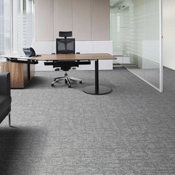 Modern office space with Mannington Scaffold Carpet Tiles in gray, covering the floor beneath a desk, chair, and glass