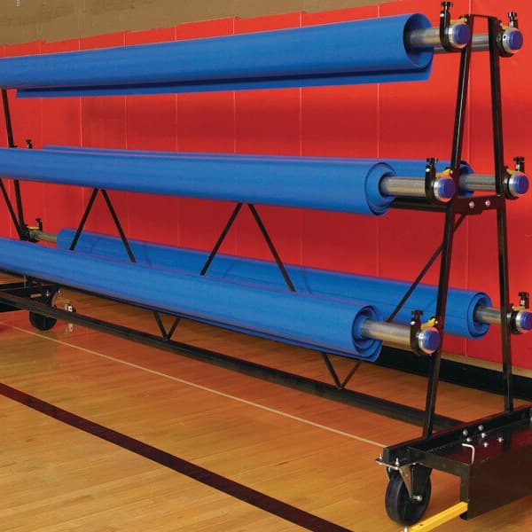 Mobile storage rack with three blue rolled mats on wheels, in a gym with hardwood flooring and red walls