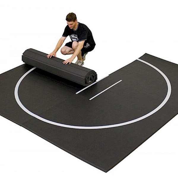 Wrestling mat being rolled up by a man on white background.