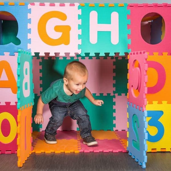 Toddler inside a rainbow foam puzzle mat structure with letters and numbers